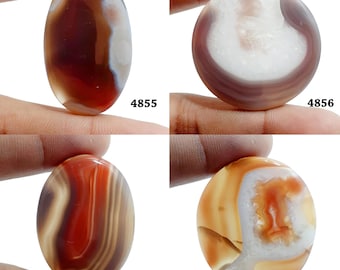 Könnte beinhalten: Vier Achat-Cabochons in verschiedenen Farben und Mustern, darunter Braun, Weiß, Rot und Orange. Die Cabochons sind oval und rund und werden in einer Hand gehalten.