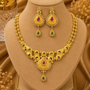 Puede incluir: Un conjunto de collar y pendientes de oro con intrincados patrones de filigrana, piedras en forma de lágrima de color rosa y verde, y pequeños acentos claros. El collar tiene un diseño de cadena de doble hebra con un colgante central.
