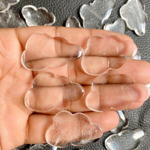 Könnte beinhalten: Eine Sammlung von klaren Quarzkristall-Wolken-Steinen. Die Steine sind glatt und poliert und liegen in einer Hand.