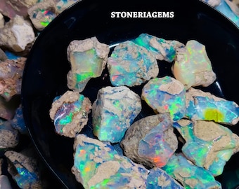 May include: A close-up of a collection of rough opal gemstones in various shades of blue, green, and white. The opals are in a black bowl and have a rough, natural texture. The text "STONERIAGEMS" is visible in the image.