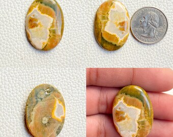 May include: Oval shaped, polished, green, brown, and white jasper cabochon gemstone. The stone has a unique pattern of swirls and veins.