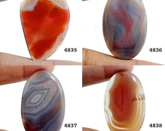 Könnte beinhalten: Vier ovale Achat-Cabochons mit unterschiedlichen Mustern und Farben. Die Cabochons sind eine Mischung aus Rot, Orange, Braun, Weiß und Grau. Die Cabochons sind mit den Nummern 4835, 4836, 4837 und 4838 gekennzeichnet.