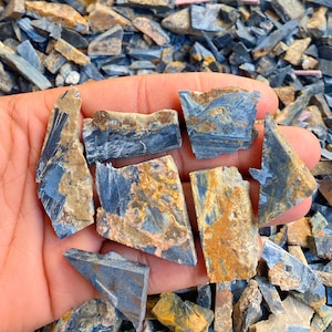 Op de afbeelding: Een verzameling blauwe tijgeroog edelsteen chips. De chips zijn in verschillende vormen en maten en hebben een mix van blauwe, gouden en bruine kleuren.
