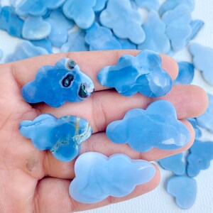 May include: A collection of blue cloud-shaped gemstones. The stones vary in shades of blue, with some displaying unique patterns and inclusions. The cloud carvings are smooth and polished, suggesting they are intended for jewelry or decorative purposes.