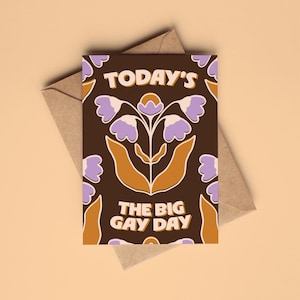 May include: A rectangular greeting card with a dark brown background featuring a repeating floral pattern in light purple and mustard yellow. The text TODAY'S THE BIG GAY DAY is printed in a bold, cream-coloured, rounded sans-serif font.