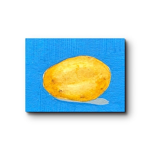 Könnte beinhalten: Ein Aquarellgemälde auf einer strukturierten Oberfläche, das eine einzelne, oval geformte gelbe Kartoffel vor einem leuchtend blauen Hintergrund zeigt. Die Kartoffel hat dezente braune Flecken und einen hellgrauen Schatten auf der blauen Fläche.