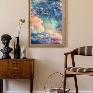 Op de afbeelding: Een ingelijste kunstdruk met een dromerige luchtsc&egrave;ne met wolken in roze, blauw en wit. Het kunstwerk wordt tentoongesteld boven een houten kast met een zwart buste, een zwarte vaas en een glazen koepel. Een houten stoel en een metalen tijdschriftenrek zijn ook zichtbaar.