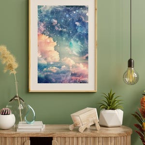 Op de afbeelding: Een ingelijste kunstdruk toont een dromerige, aquarelachtige hemelse sc&egrave;ne. Het kunstwerk toont een mix van roze, blauwe en witte tinten, met pluizige wolken en een sterrenhemel. De lijst heeft een lichte houtkleur en de print wordt op een groene muur weergegeven.