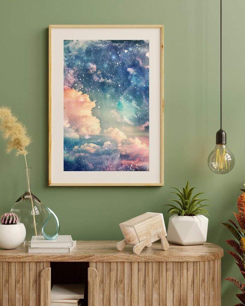 Op de afbeelding: Een ingelijste kunstdruk toont een dromerige, aquarelachtige hemelse sc&egrave;ne. Het kunstwerk toont een mix van roze, blauwe en witte tinten, met pluizige wolken en een sterrenhemel. De lijst heeft een lichte houtkleur en de print wordt op een groene muur weergegeven.