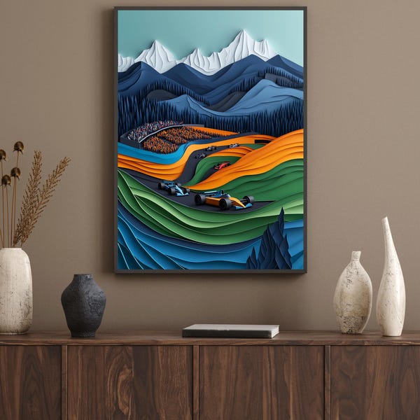 May include: A framed paper art print depicting a race car track winding through a mountainous landscape. The mountains are layered in shades of blue and white, with green trees and a crowd of people in the background. The race cars are orange and blue, and the track is outlined in blue.