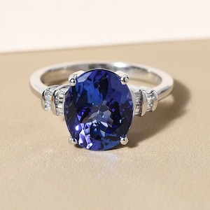 Può includere: Un anello d'argento con una grande pietra preziosa blu di forma ovale circondata da piccole pietre preziose chiare.