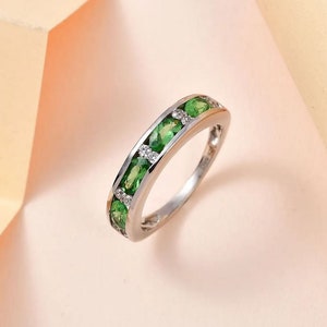 Puede incluir: Un anillo de banda de plata con una fila de piedras preciosas verdes ovaladas y piedras preciosas transparentes más pequeñas.