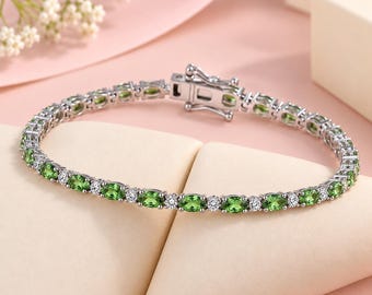 Puede incluir: Una pulsera de tenis en tono plateado que presenta un patrón repetitivo de piedras preciosas verdes de corte ovalado alternadas con pequeñas piedras blancas redondas y transparentes. Incluye un cierre de caja seguro con pestillo.