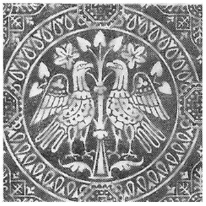 Może przedstawiać: Czarno-białe zdjęcie przedstawiające okrągły wz&oacute;r z dwoma stylizowanymi ptakami, kt&oacute;re patrzą na siebie z rozpostartymi skrzydłami. Ptaki siedzą na drzewie z liśćmi. Wz&oacute;r jest otoczony okręgiem powtarzających się wzor&oacute;w.