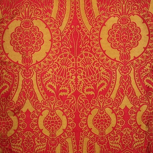 K&ouml;nnte beinhalten: Ein roter Stoff mit einem goldenen Muster aus komplizierten floralen Designs. Das Muster ist symmetrisch und weist sich wiederholende Motive auf.