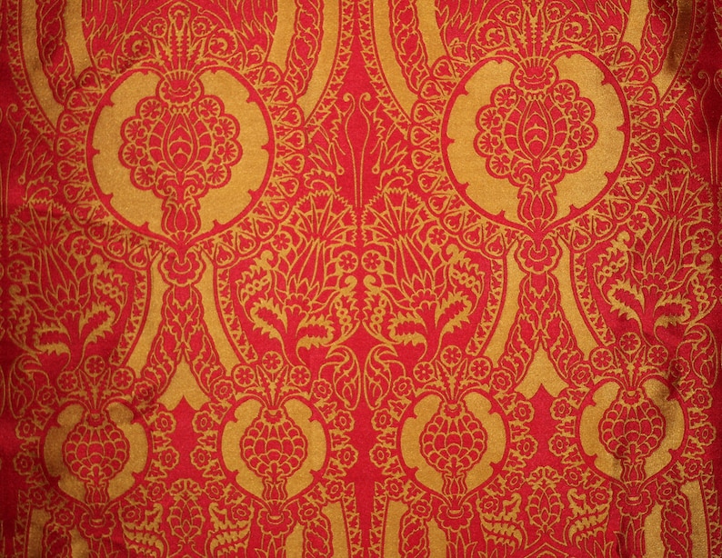 K&ouml;nnte beinhalten: Ein roter Stoff mit einem goldenen Muster aus komplizierten floralen Designs. Das Muster ist symmetrisch und weist sich wiederholende Motive auf.