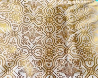 Pode incluir: Tecido branco com um padrão repetido de anjos dourados com asas e desenhos florais ornamentados.