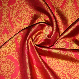 K&ouml;nnte beinhalten: Roter Stoff mit goldfarbenem Paisley-Muster. Der Stoff ist gefaltet und drapiert und zeigt die Textur und den Glanz des Materials.