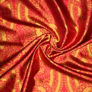 K&ouml;nnte beinhalten: Roter Stoff mit goldfarbenem Paisley-Muster. Der Stoff ist drapiert und gefaltet, wodurch die Textur und der Glanz des Materials sichtbar werden.