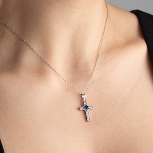 May include: A silver chain necklace with a small cross pendant. The cross is adorned with clear and blue gemstones.