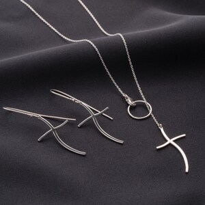 Op de afbeelding: Een set zilveren sieraden met een delicate ketting met een klein rond hangertje en een kruisbedel, en een paar bijpassende oorbellen met gebogen kruisontwerpen.