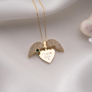Peut inclure: Un collier dor&eacute; avec un pendentif en forme de c&oelig;ur et des ailes d'ange. Le pendentif porte l'inscription "I Love You". Les ailes sont incrust&eacute;es de petites pierres transparentes. Une petite pierre verte est sertie &agrave; la base des ailes.
