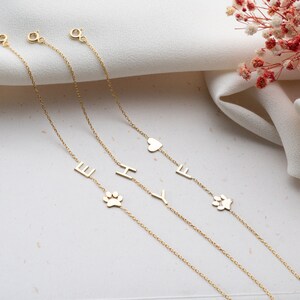 Puede incluir: Tres pulseras de cadena de oro con diferentes dijes. Los dijes incluyen un coraz&oacute;n, una huella de pata y las letras E, H e Y.