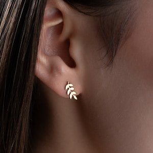 May include: A pair of gold leaf earrings. The earrings are small and delicate, and they feature a simple design of a branch with leaves.