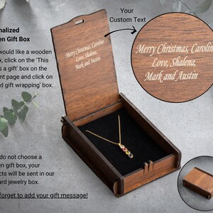 Peut inclure: Coffret cadeau en bois ouvert, r&eacute;v&eacute;lant un collier en or avec des pierres pr&eacute;cieuses color&eacute;es sur un int&eacute;rieur en velours noir. Le couvercle porte l'inscription "Merry Christmas, Caroline Love, Shalena, Mark and Austin."
