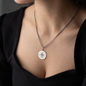 May include: A silver necklace with a compass pendant. The compass is a circular design with a star in the center and lines radiating out from the star.