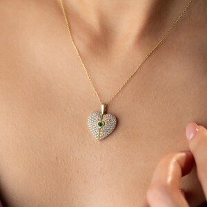 Peut inclure: Un collier dor&eacute; avec un pendentif en forme de c&oelig;ur. Le pendentif est incrust&eacute; de petites pierres claires et d'une pierre verte au centre. Le collier est port&eacute;, avec la cha&icirc;ne visible.