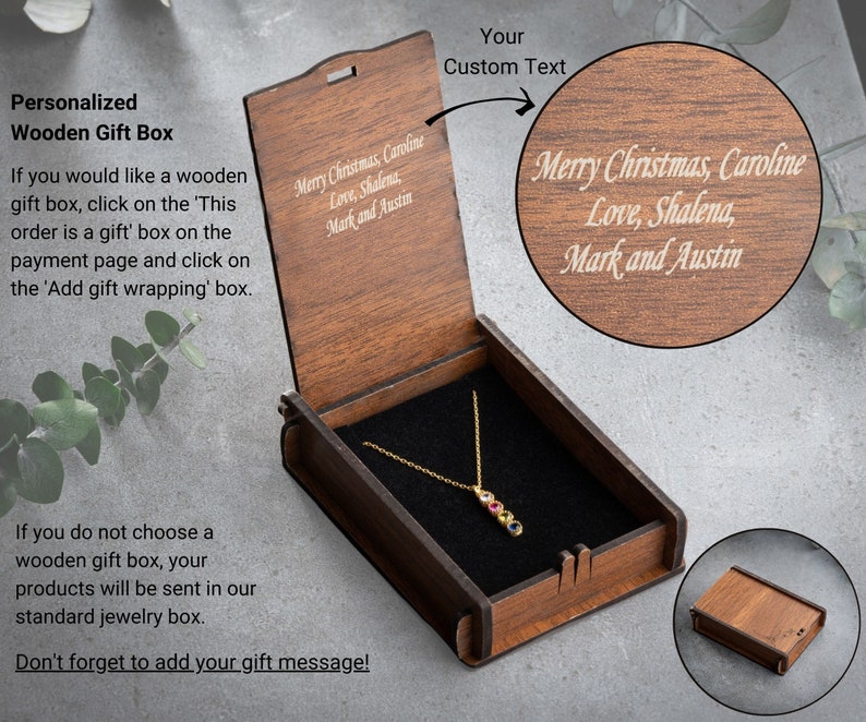 May include: A wooden gift box with a hinged lid. The lid is engraved with the text "Merry Christmas, Caroline Love, Shalena, Mark and Austin". The box is open and a gold necklace with a multi-colored gemstone pendant is inside.