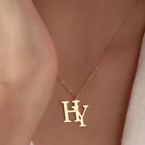 Könnte beinhalten: Eine goldfarbene Halskette mit dem Anhänger "HY". Der Anhänger ist an einer feinen Kette befestigt. Die Halskette wird getragen, und der Hintergrund ist unscharf.