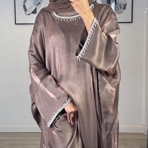 May include: A long, flowing, brown satin abaya with a sparkly, beaded trim around the neckline and sleeves.
