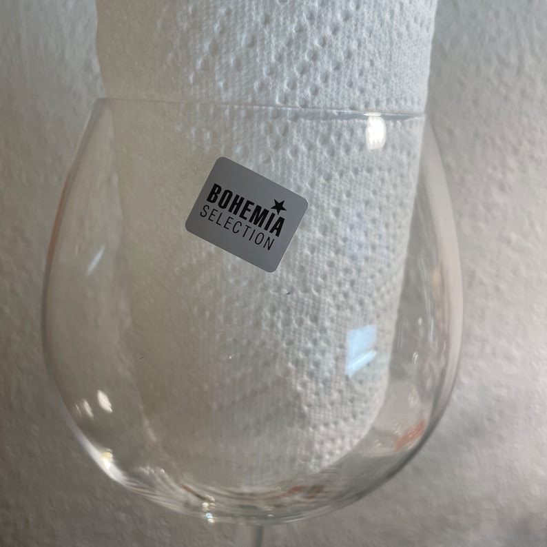May include: A clear glass wine glass with a round bowl and a stem. The glass has a sticker on it that says "BOHEMIA SELECTION" with a star.
