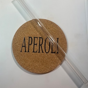 May include: A clear glass drinking straw on a cork coaster with the word "APEROL" printed on it.