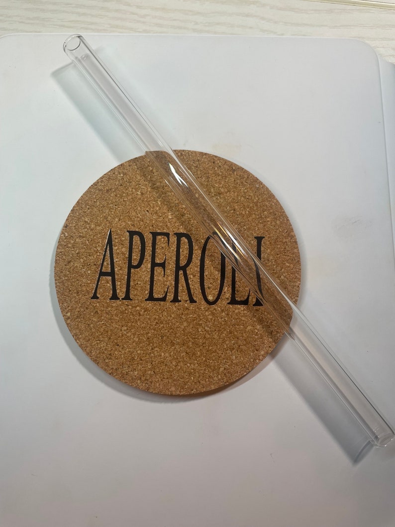 May include: A clear glass drinking straw on a cork coaster with the word "APEROL" printed on it.