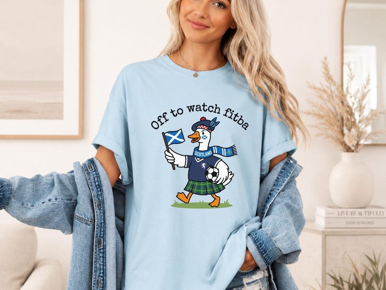 Chambray blue t-shirt mockup worn by a woman, featuring a Scottish goose football fan design with “Off to watch fitba” text and Scotland scarf graphic.
