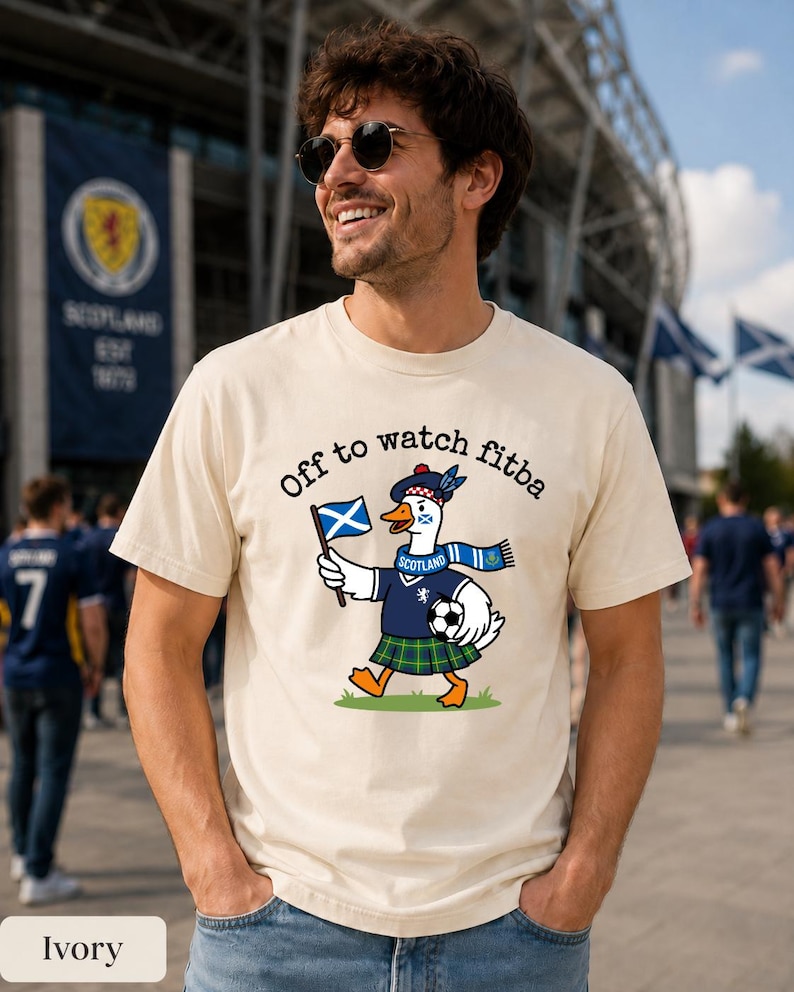 Ivory Comfort Colors style t-shirt flat lay featuring a Scotland goose soccer fan graphic with “Off to watch fitba” text, styled with neutral boho decor.