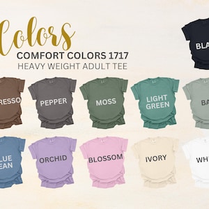 May include: A display of Comfort Colors 1717 Heavy Weight Adult Tees in various colors, including Espresso, Pepper, Moss, Light Green, Bay, Blue Jean, Orchid, Blossom, Ivory, White, and Black. The word "Colors" is written in a script font.