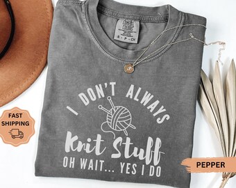 May include: A gray Comfort Colors t-shirt with the text "I DON'T ALWAYS Knit Stuff OH WAIT... YES I DO" in white. The shirt features a graphic of yarn and knitting needles. A gold necklace rests on the shirt.