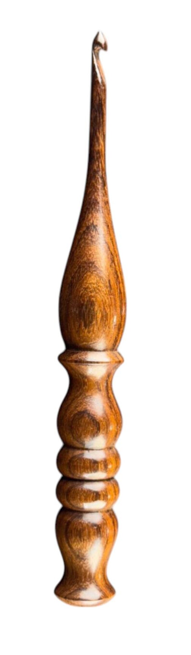 May include: A handcrafted crochet hook made of wood. The hook features a curved tip and a detailed, textured handle with a warm, brown color. The handle has a bulbous shape with a series of rounded sections.