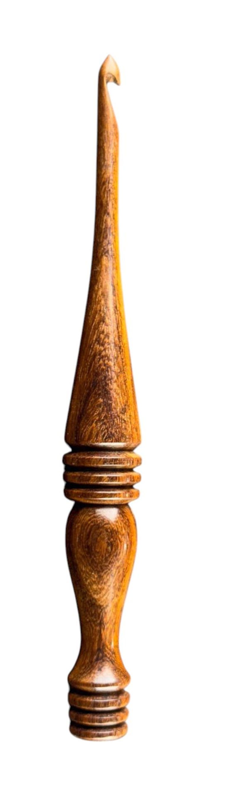 May include: A handcrafted wooden crochet hook with a curved hook end. The hook features a detailed, ergonomic design with a conical midsection and a rounded base, all crafted from warm-toned wood.