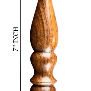 May include: A 7-inch wooden crochet hook with a curved hook end. The hook has a decorative, textured handle with a series of rounded sections. The wood grain is visible, showing shades of brown and tan.