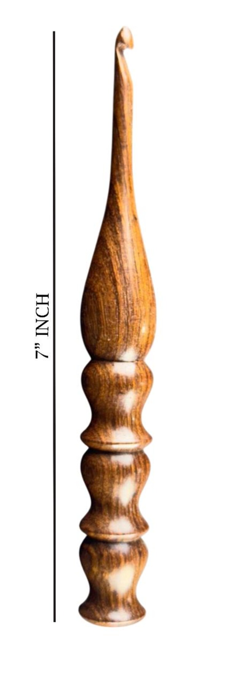 May include: A 7-inch wooden crochet hook with a curved hook end. The hook has a decorative, textured handle with a series of rounded sections. The wood grain is visible, showing shades of brown and tan.