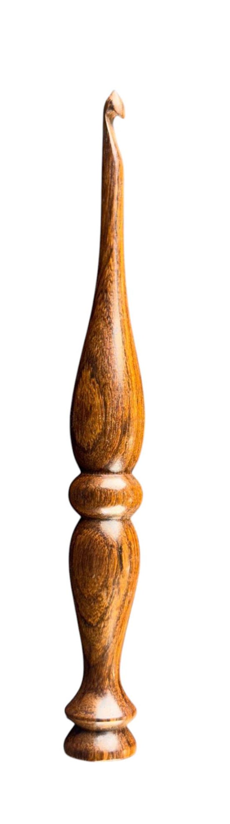 May include: A handcrafted wooden crochet hook with a polished finish. The hook features a curved end for catching yarn and a detailed, ergonomic handle. The wood grain is visible, showcasing the natural beauty of the material.