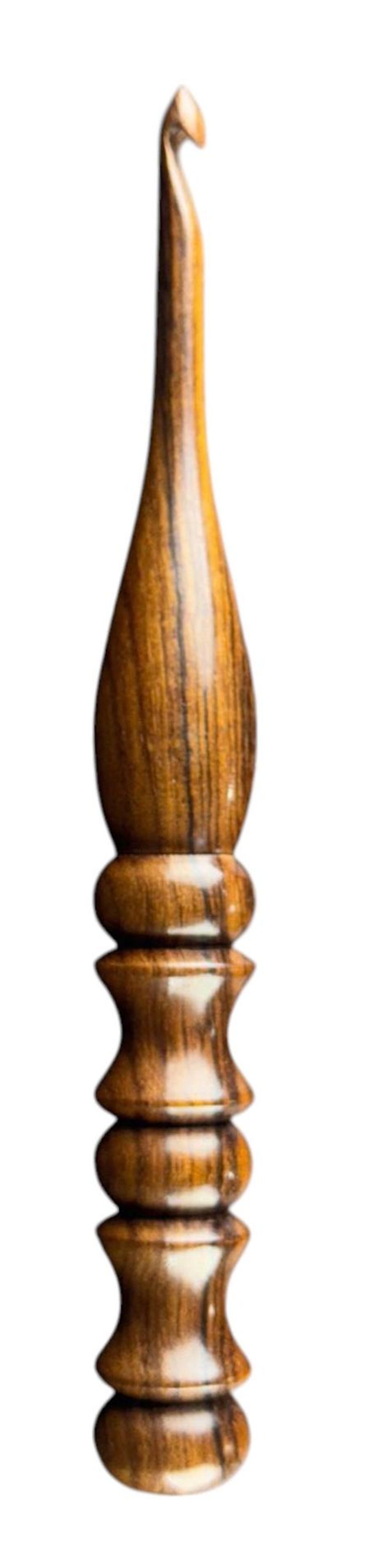 May include: A handcrafted wooden crochet hook with a polished finish. The hook features a curved head and a decorative handle with a series of rounded and stacked sections. The wood grain is visible.