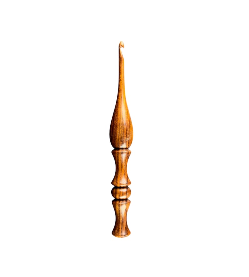 May include: A handcrafted wooden crochet hook with a polished, warm brown finish. The hook features a slender, elongated neck and a detailed, decorative handle. The hook is designed for yarn crafts and is set against a clean white background.