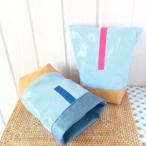 May include: Two striped fabric storage bags with brown leather trim. One bag has a pink stripe and the other has a blue stripe.