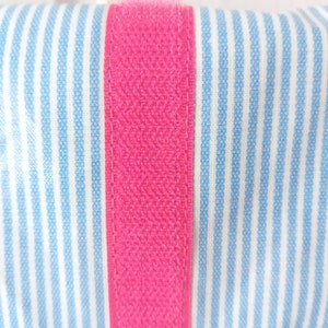 May include: Close-up of a pink fabric strip sewn onto a blue and white striped fabric. The fabric has a textured appearance.